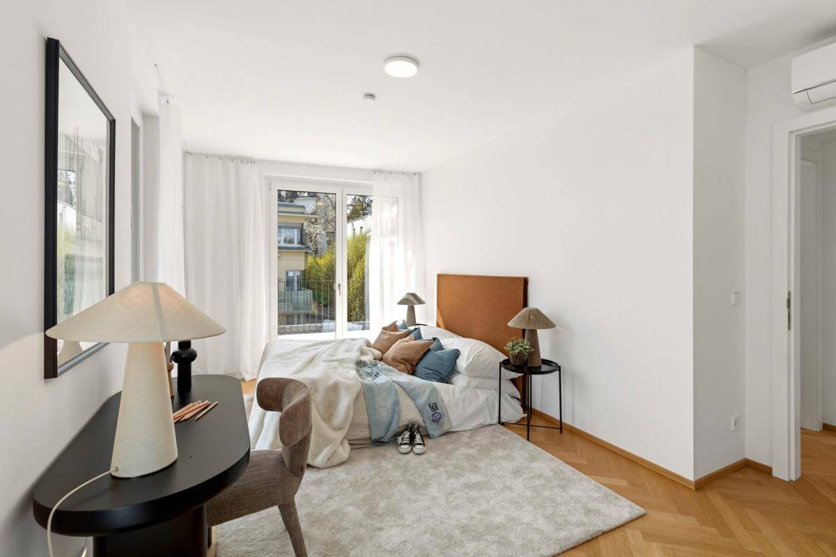 Gemütliches Schlafzimmer mit Parkettboden, großem Bett und Zugang zum Balkon mit Blick ins Grüne.