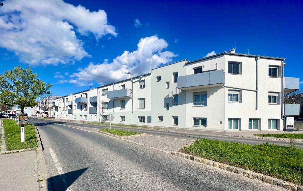 Moderne Wohnanlage mit weißer Fassade und grauen Balkonen entlang einer Straße unter blauem Himmel.
