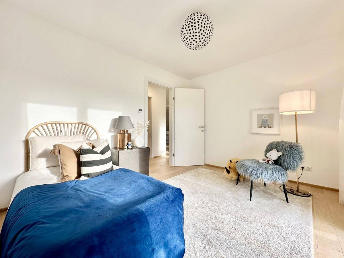 Helles Kinder- oder Gästezimmer mit Einzelbett, flauschigem Stuhl und Teppichboden.