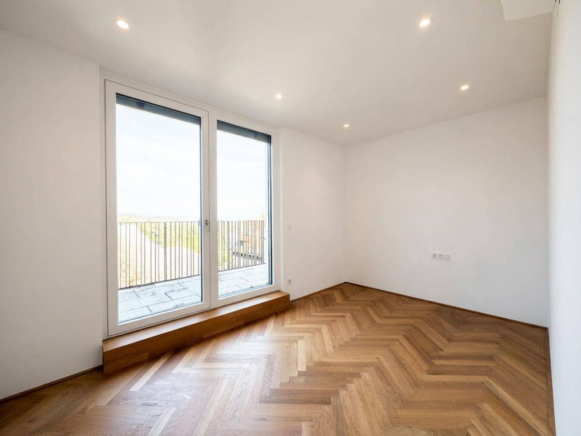 Helles Zimmer mit Fischgrätparkett und bodentiefen Fenstern, die auf einen Balkon führen.