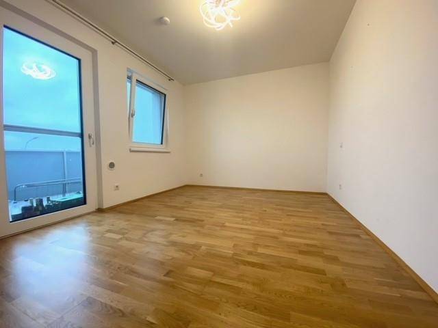 Schlafzimmer mit hellem Parkettboden und Zugang zu einem Außenbereich durch eine Glastür.