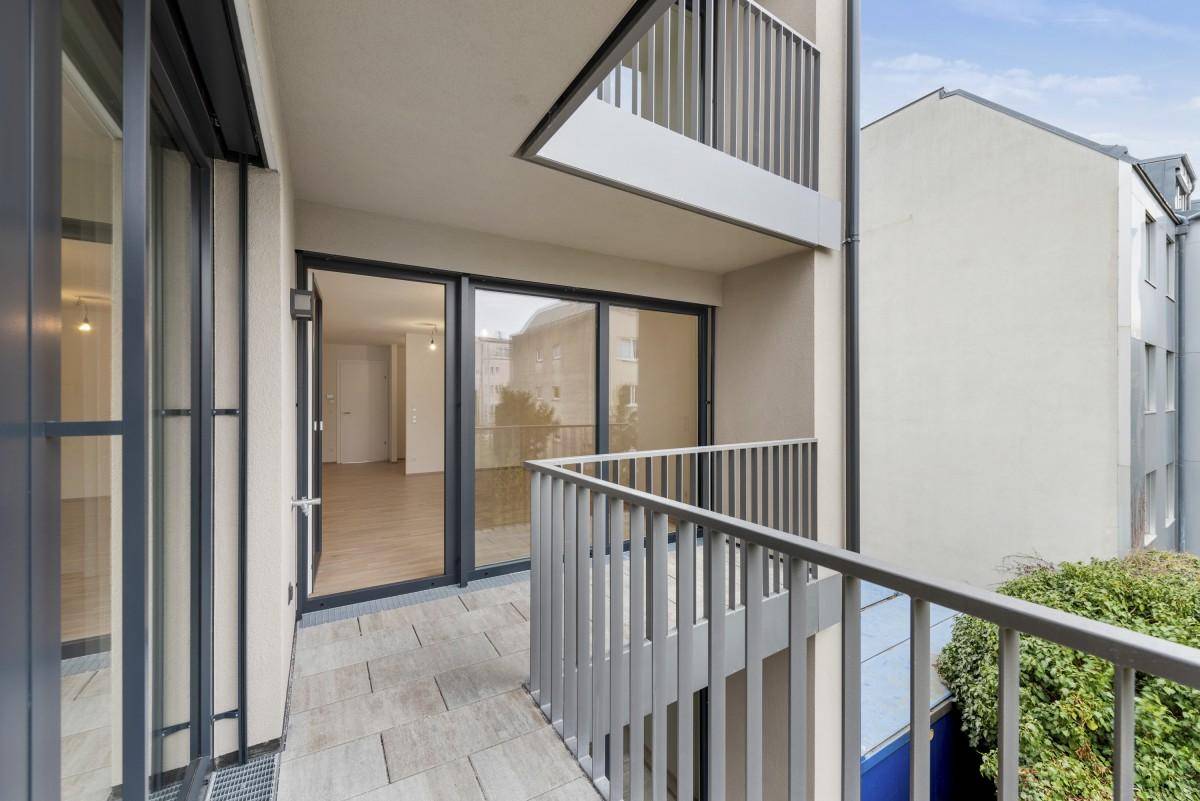 Moderner Balkon mit Fliesenboden und Metallgeländer, verbunden mit dem Innenbereich.