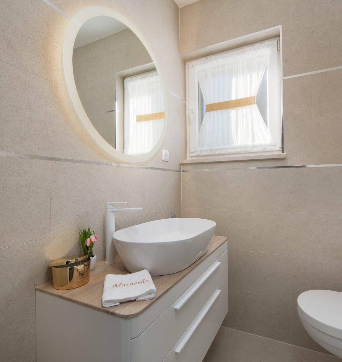 Modernes Badezimmer mit ovalem Aufsatzwaschbecken, beleuchtetem Spiegel und beigen Fliesen.