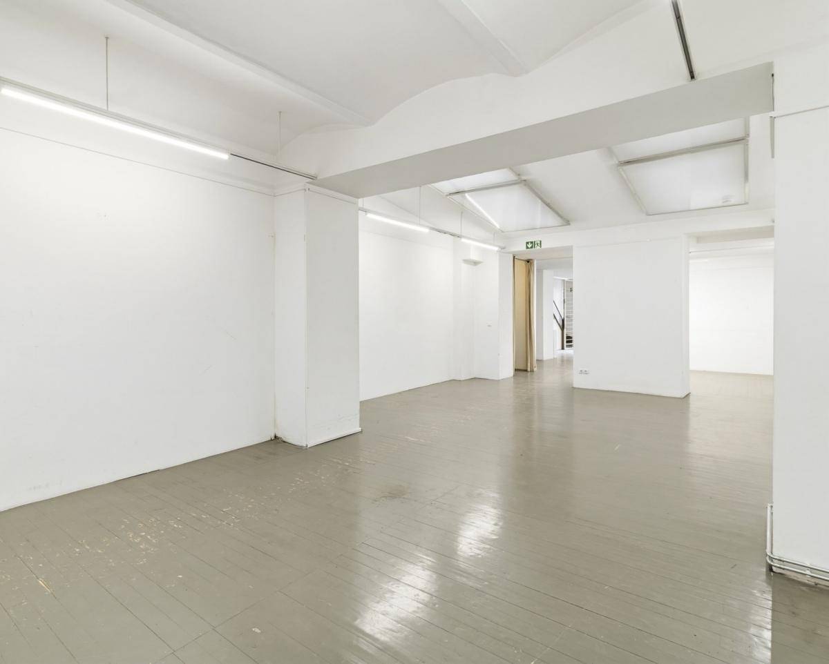 Geräumiger, leerer Gewerberaum mit grau gestrichenem Holzboden und weißen Wänden, bietet viel Platz.