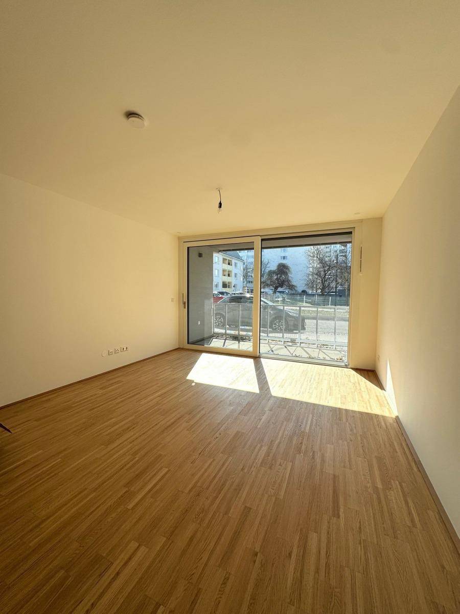 Lichtdurchflutetes Wohnzimmer mit Holzboden und großer Schiebetür zum Balkon.