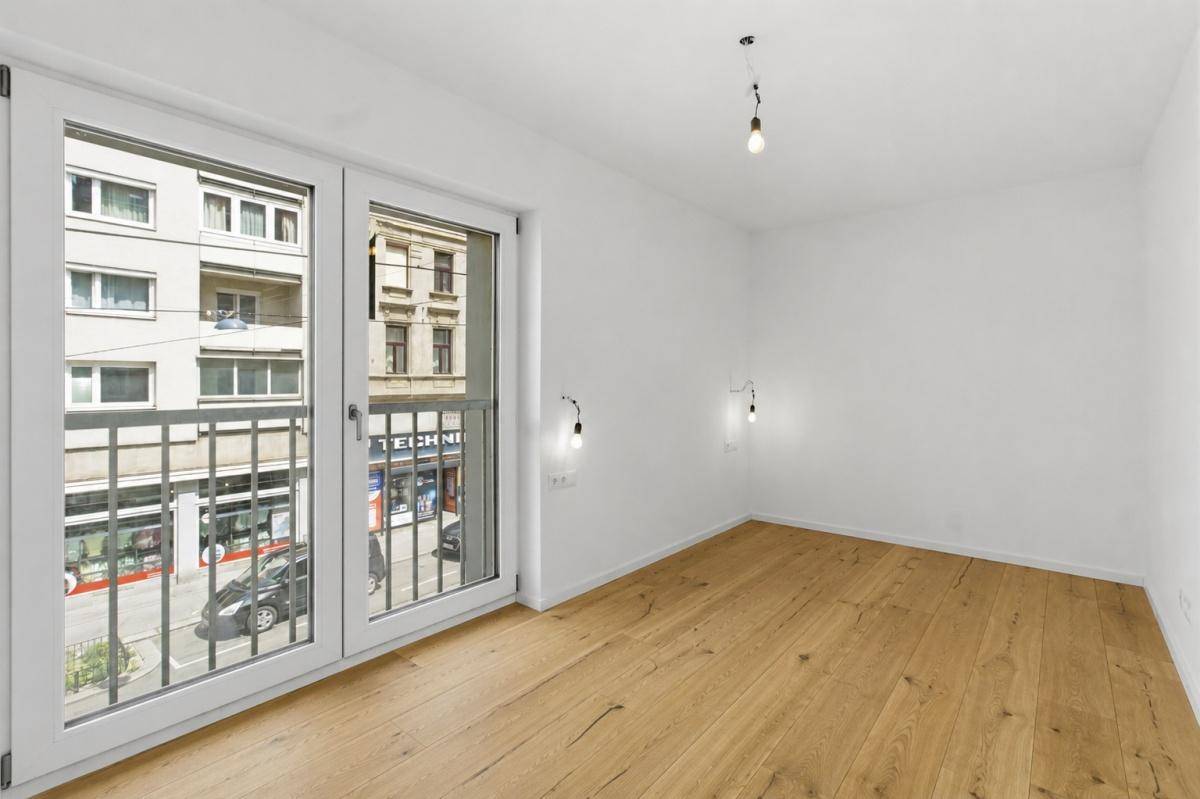 Heller Raum mit Parkettboden und französischem Balkon mit Blick auf die Straße.