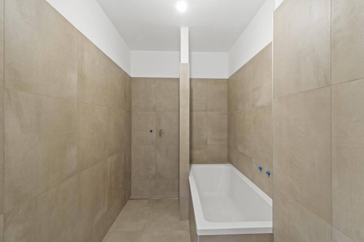 Unfertiges Badezimmer mit beigefarbenen Fliesen an Wänden und Boden sowie einer eingebauten Badewanne.