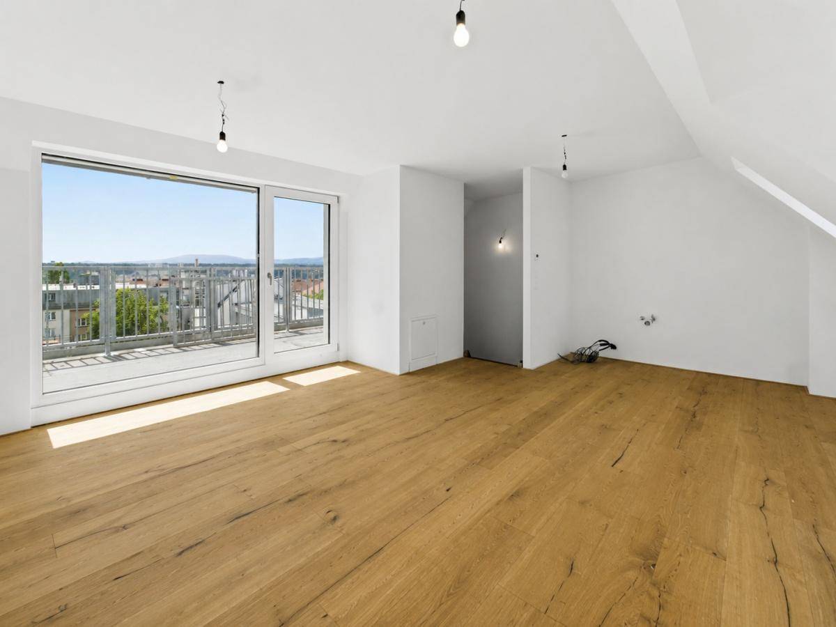 Lichtdurchfluteter Dachgeschossraum mit Holzboden und breiter Fensterfront, die den Blick nach draußen öffnet.