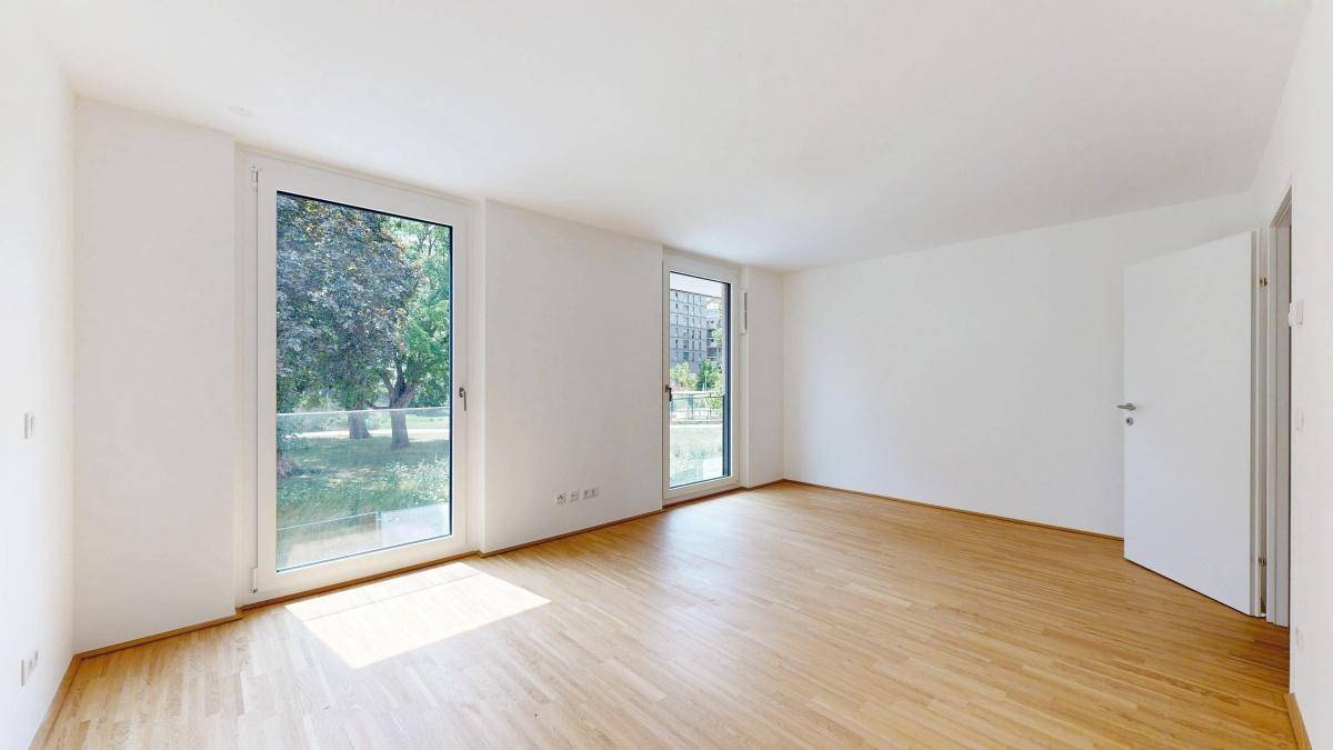 Lichtdurchfluteter Raum mit großen Fenstern und Parkettboden, ideal als Wohnzimmer.