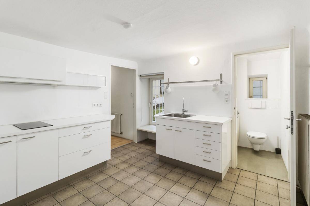 Kleine, weiße Küchenzeile mit Spüle, Kochfeld und angrenzender Toilette, funktional und kompakt.
