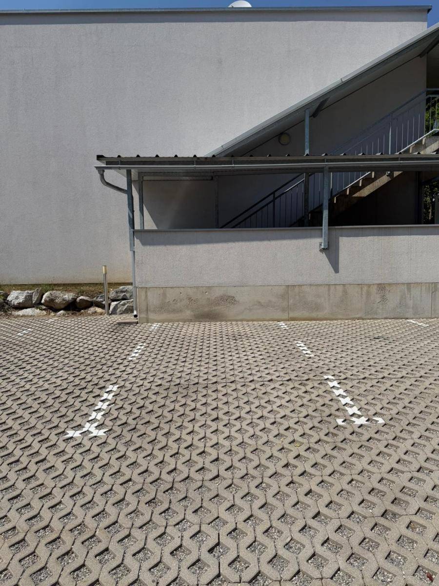 Detailansicht des Außenparkplatzes mit Markierungen und der modernen Gebäudefassade mit Außentreppe.