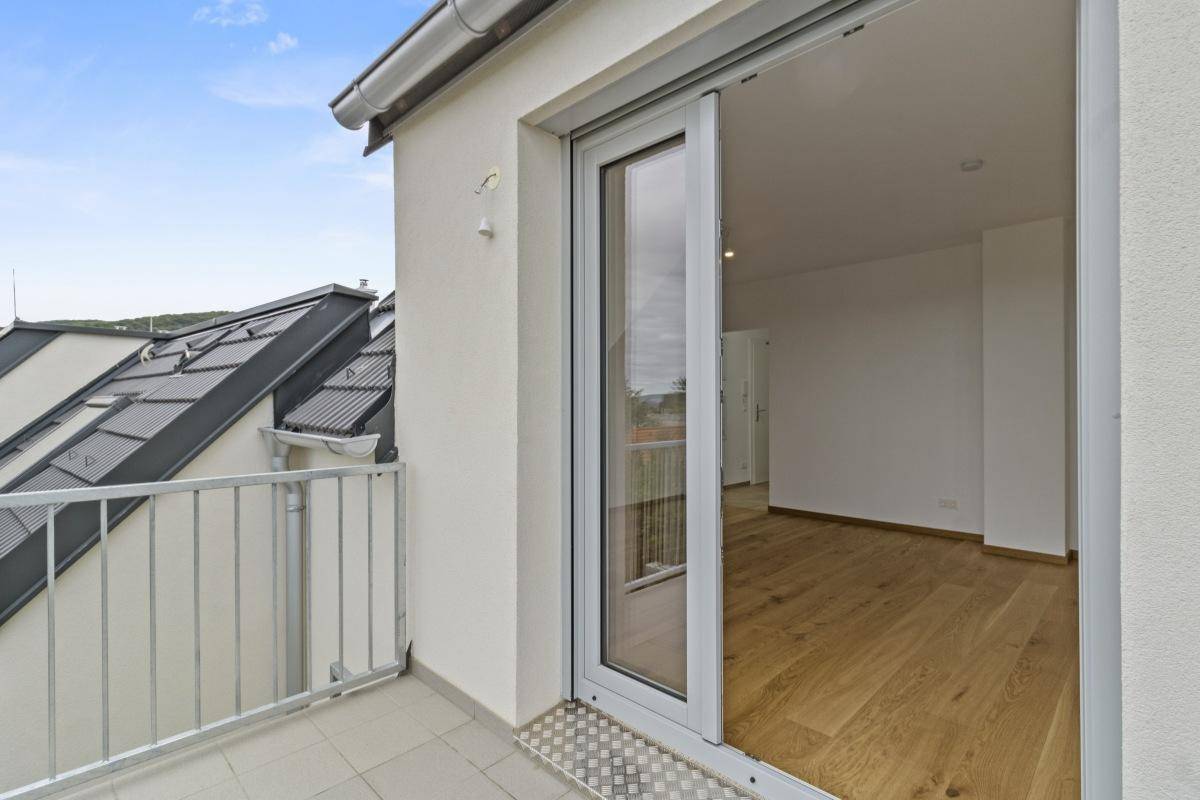 Blick vom Balkon in einen hellen, leeren Raum mit Holzboden und großer Glasschiebetür.