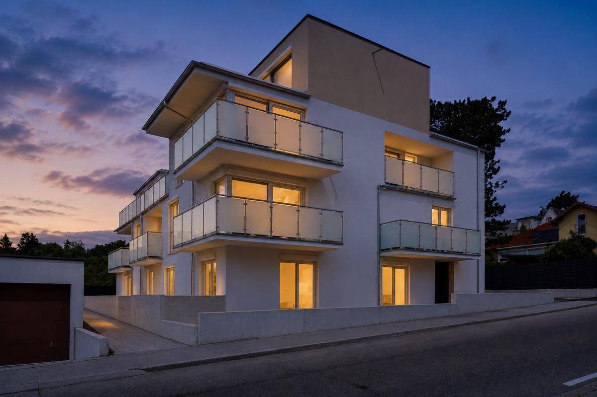 Modernes Wohngebäude bei Sonnenuntergang mit beleuchteten Balkonen und Fenstern.