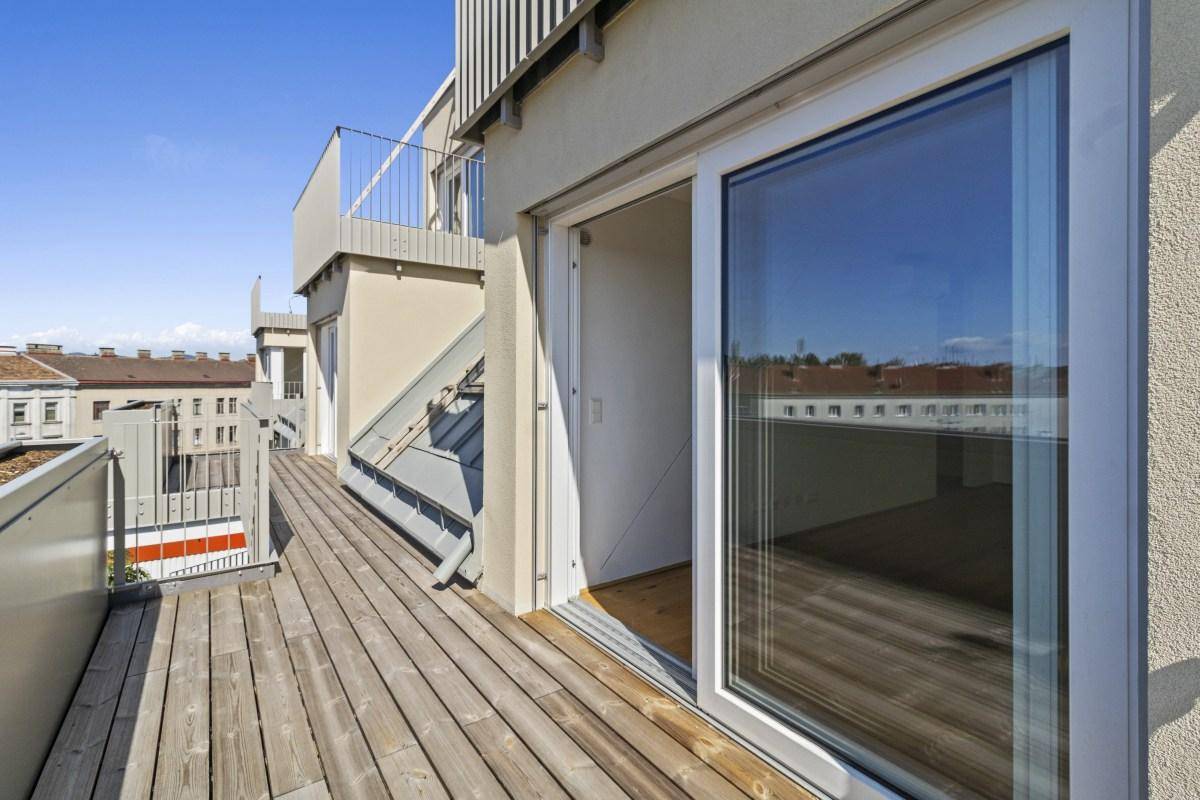 Geräumiger Balkon mit Holzboden und Zugang zu einem hellen Innenraum.