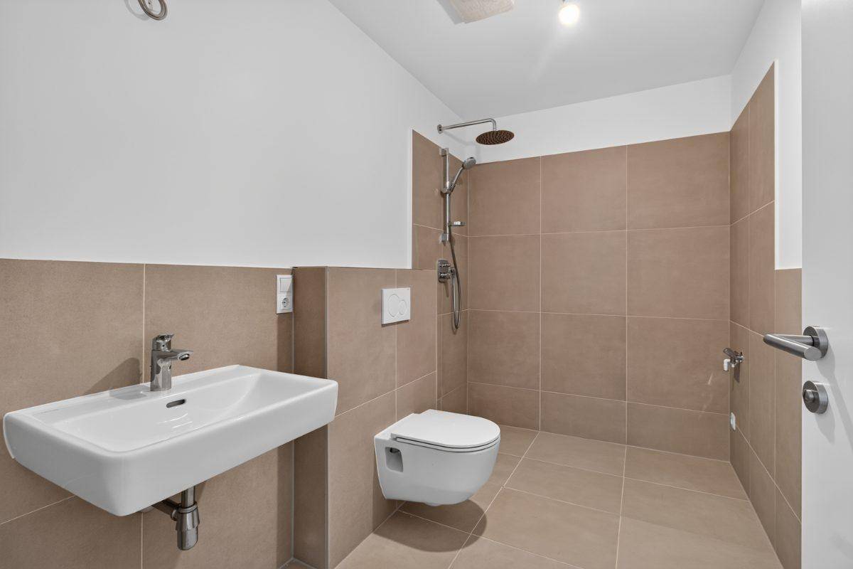 Modernes Badezimmer mit beigefarbenen Fliesen, Dusche und wandhängendem WC.