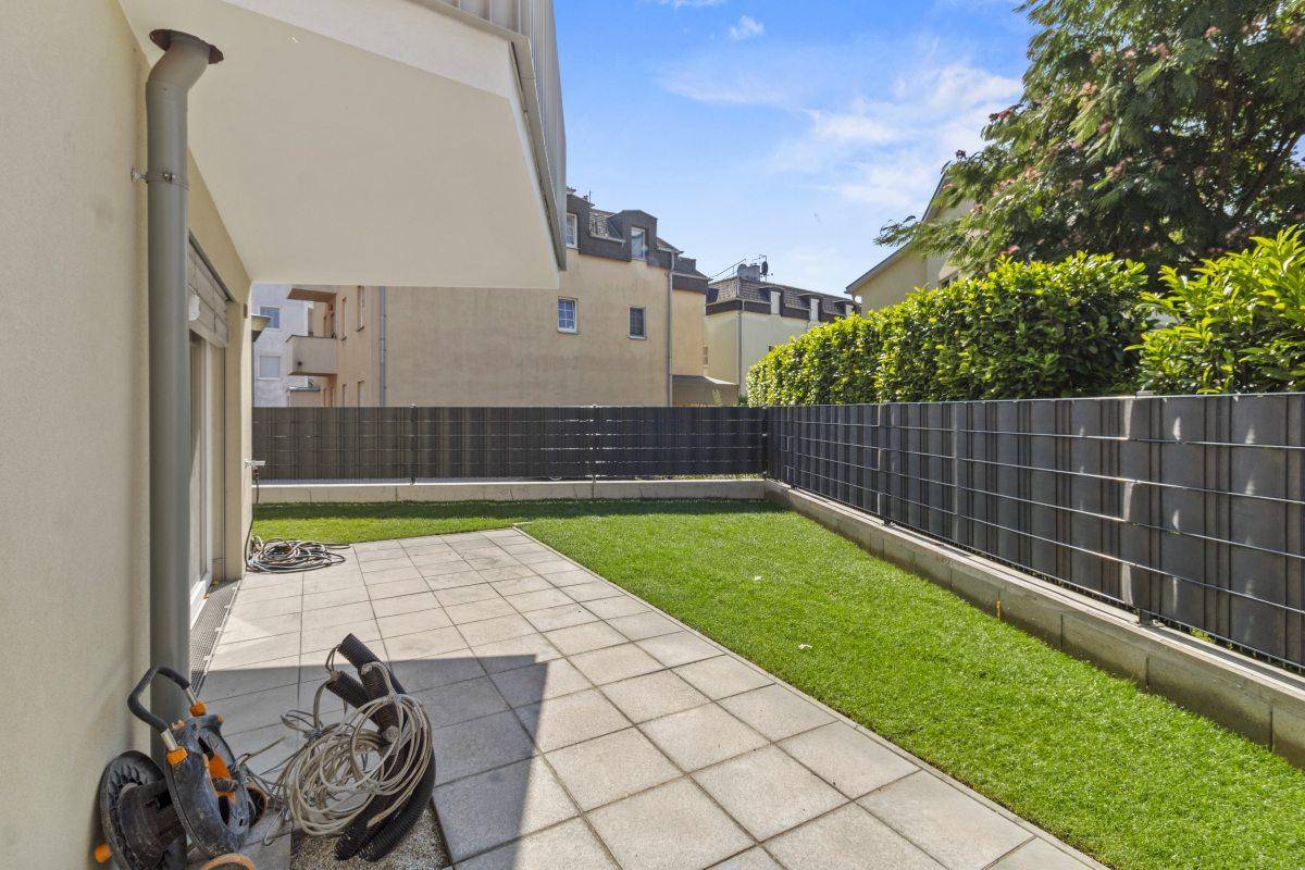 Terrasse und Gartenbereich mit Rasenfläche, umgeben von einer modernen Zaunanlage und Hecke.