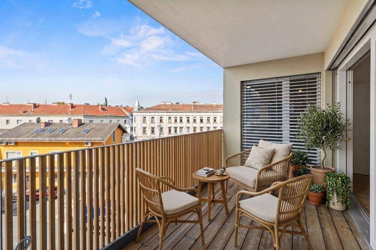 Gemütlicher Balkon mit Holzfußboden, Rattanmöbeln und Blick über die städtische Umgebung.