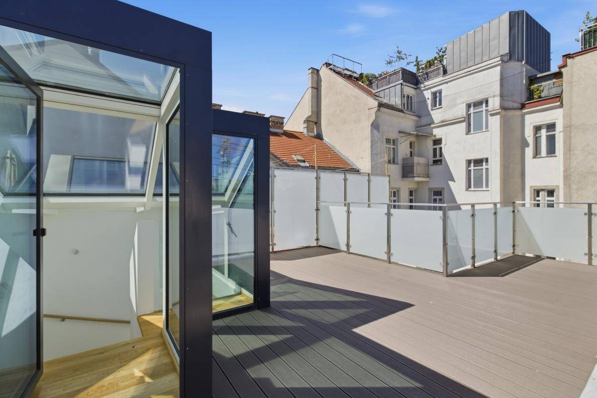 Dachterrasse mit elegantem Glaszugang zum Innenbereich und Holzbelag unter blauem Himmel.