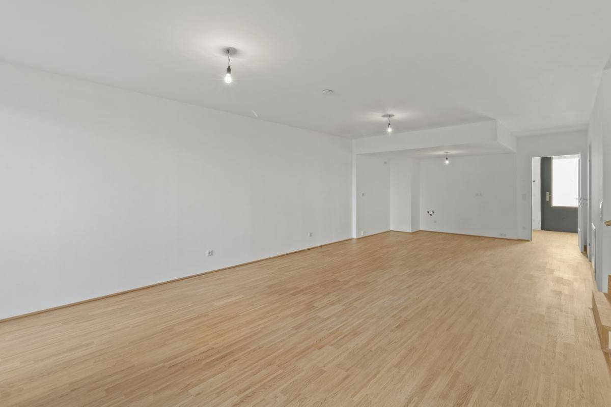 Heller, unmöblierter Wohnraum mit Holzboden und weiß gestrichenen Wänden, bereit zum Einzug.