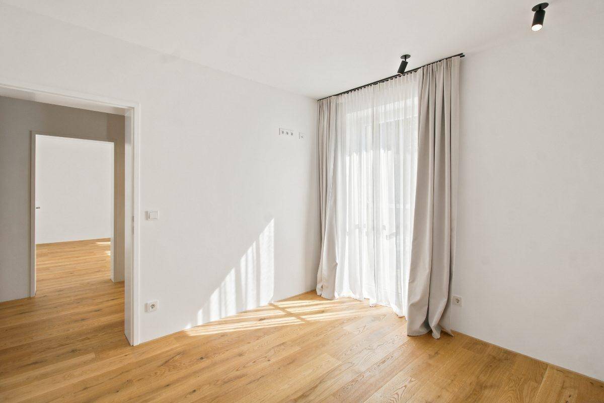 Helles Schlafzimmer mit Holzboden, großem Fenster und eleganten Vorhängen.