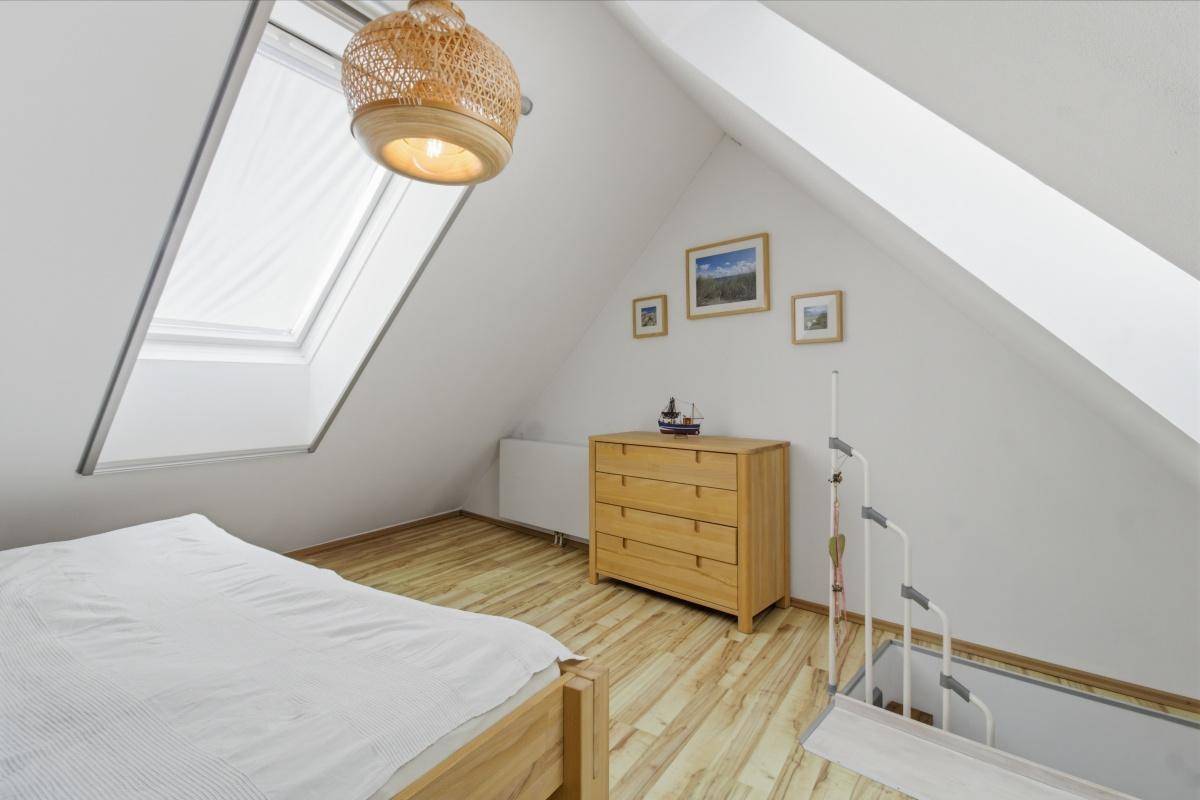 Helles Schlafzimmer im Dachgeschoss mit Kommode, Laminatboden und einem Dachfenster.