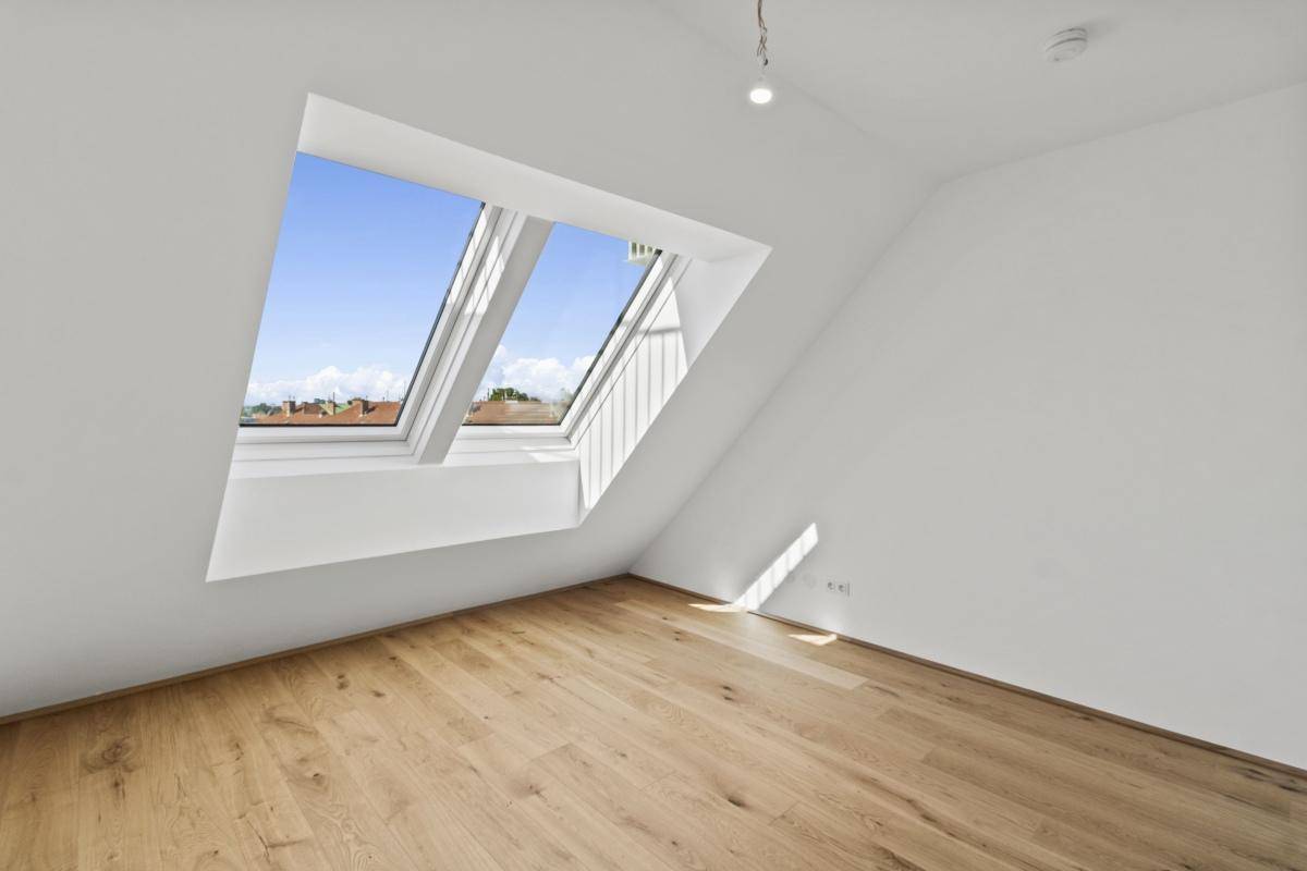 Lichtdurchflutetes Dachzimmer mit Holzboden und schrägen Wänden, ideal für ein Schlafzimmer.