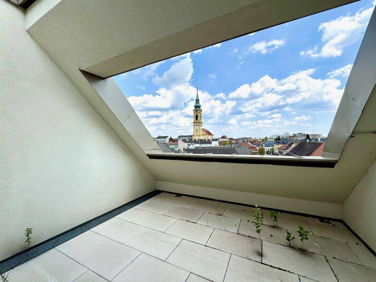 Dachterrasse mit hellen Fliesen und einem beeindruckenden Blick auf die Stadt und einen historischen Kirchturm.