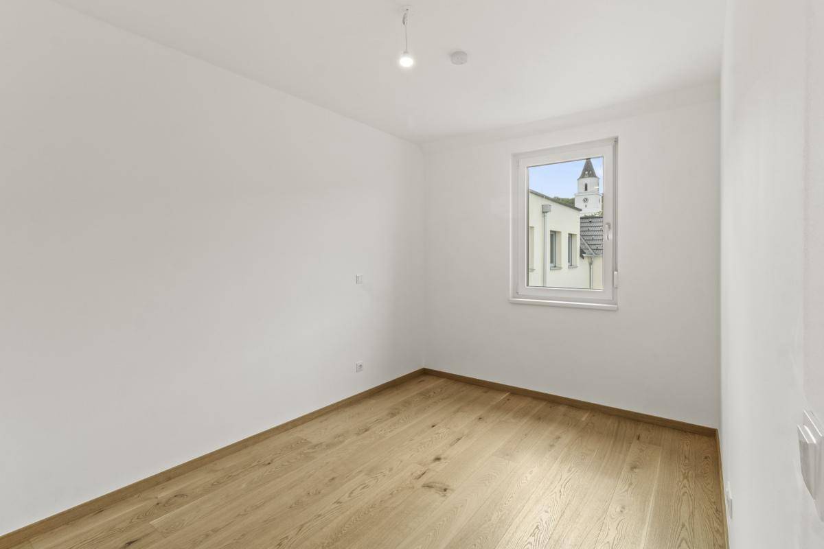 Helles Schlafzimmer mit Holzboden, weißen Wänden und Blick auf einen Kirchturm.