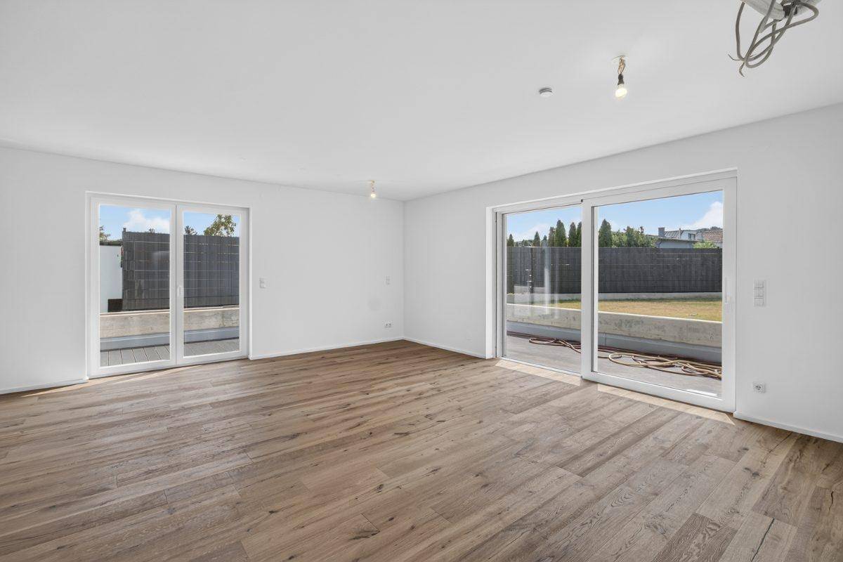 Großzügiger Wohnraum mit Holzboden und zwei großen Fensterfronten für viel Tageslicht.