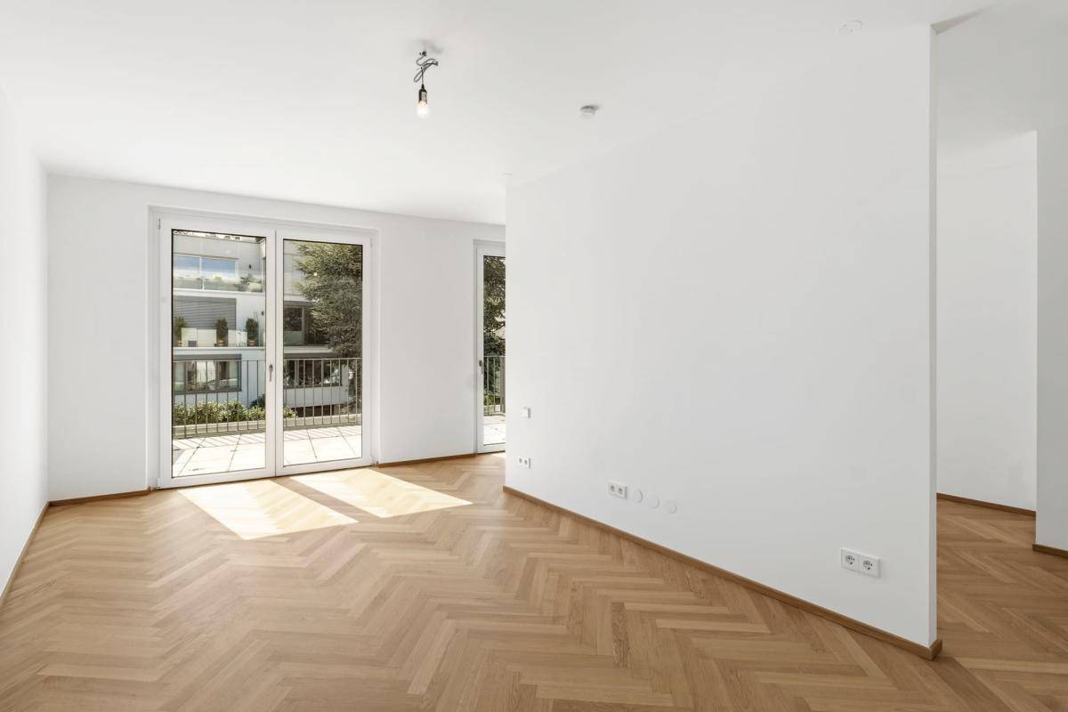 Heller Wohnraum mit Fischgrätparkett und Zugang zu einem Balkon mit Blick ins Grüne.