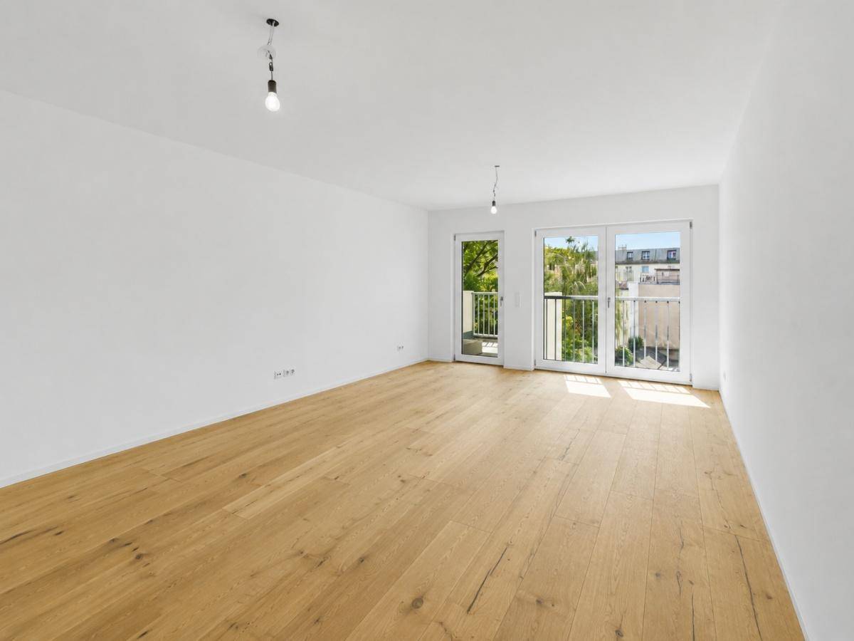 Lichtdurchfluteter Wohnraum mit hellem Holzboden und Zugang zu zwei französischen Balkonen.