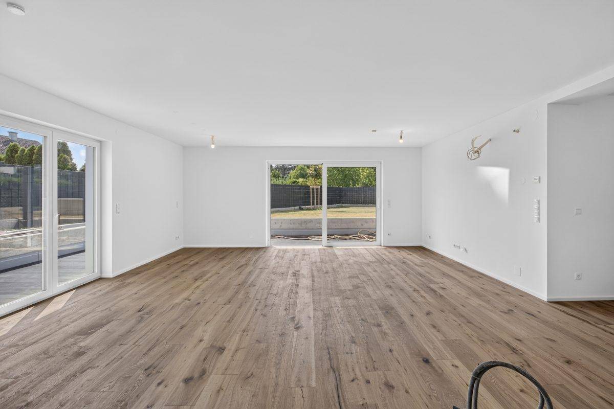 Lichtdurchflutetes Wohnzimmer mit Holzboden und breiten Schiebetüren, die zum Außenbereich führen.