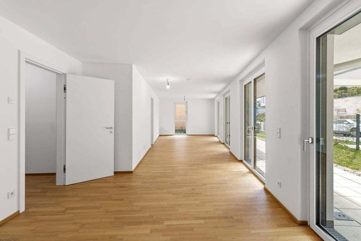 Geräumiger, unmöblierter Wohnbereich mit viel Tageslicht und hellem Parkettboden.