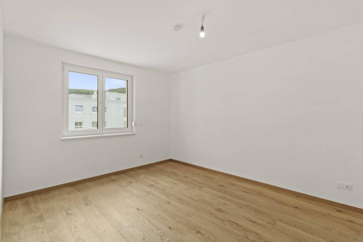 Leeres Schlafzimmer mit Holzparkettboden und einem Fenster, das Tageslicht spendet.