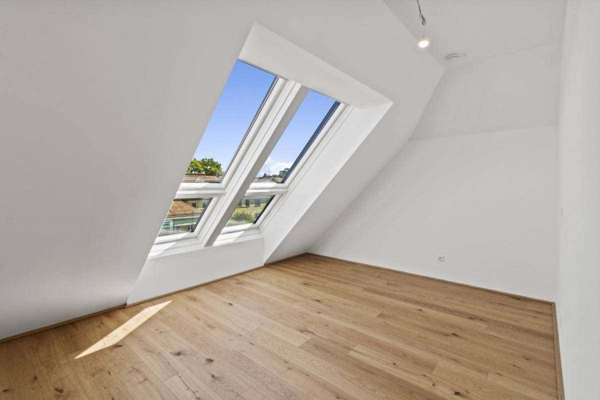 Lichtdurchfluteter Dachgeschossraum mit Holzboden und großen Dachfenstern, die den Raum erhellen.