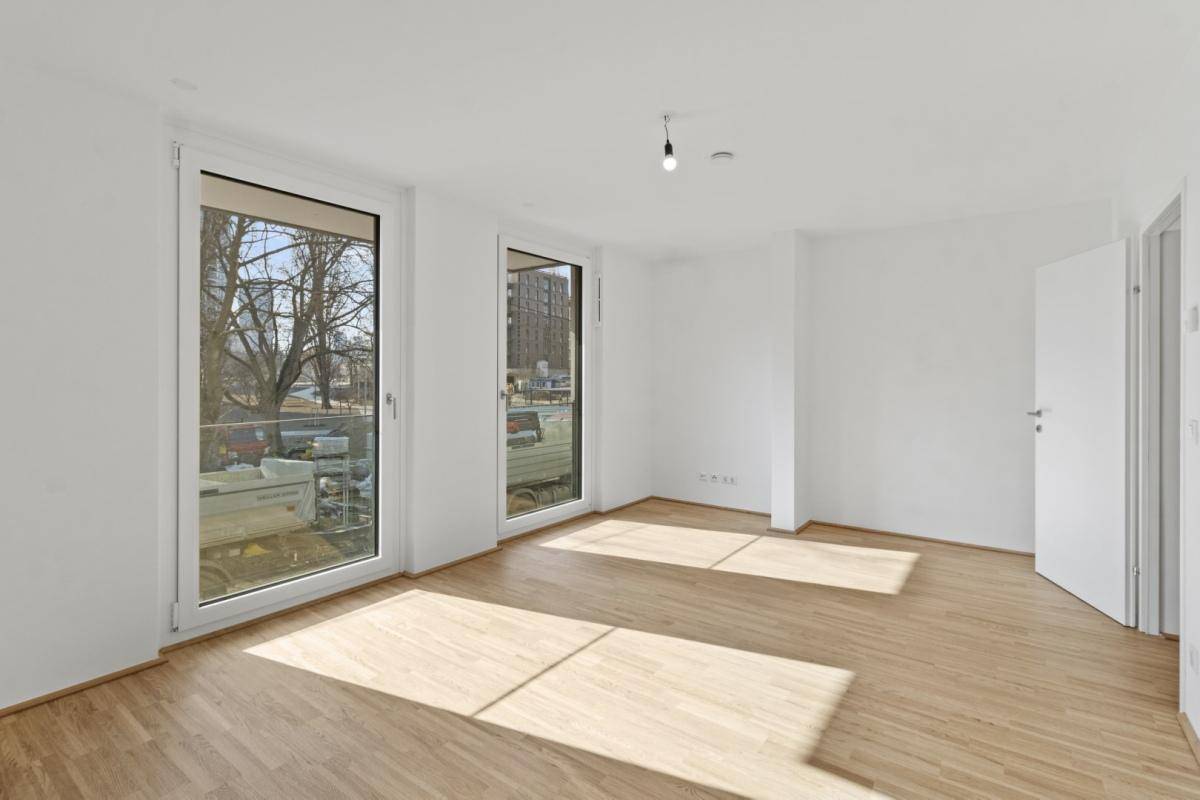 Geräumiger, heller Raum mit Holzboden und viel Tageslicht durch große Fenstertüren.
