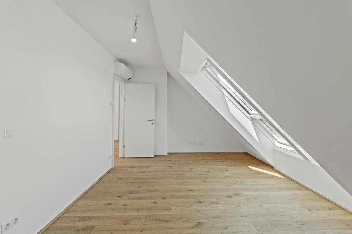 Heller Raum im Dachgeschoss mit Holzboden, schräger Wand und einem Dachfenster.