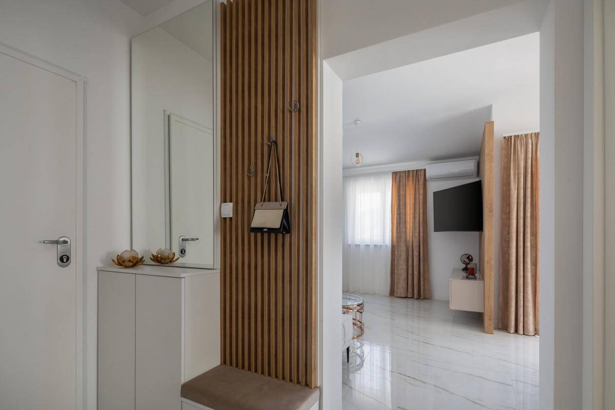 Heller Eingangsbereich mit Garderobe, Spiegel und Holzakzenten, der zum Wohnbereich führt.