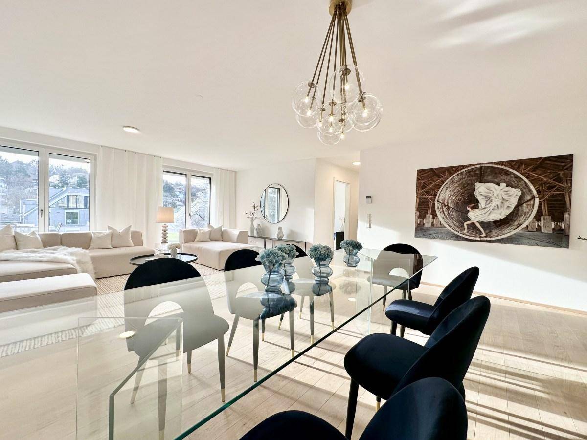 Eleganter Essbereich mit Glastisch und blauen Samtstühlen, offen zum hellen Wohnbereich.