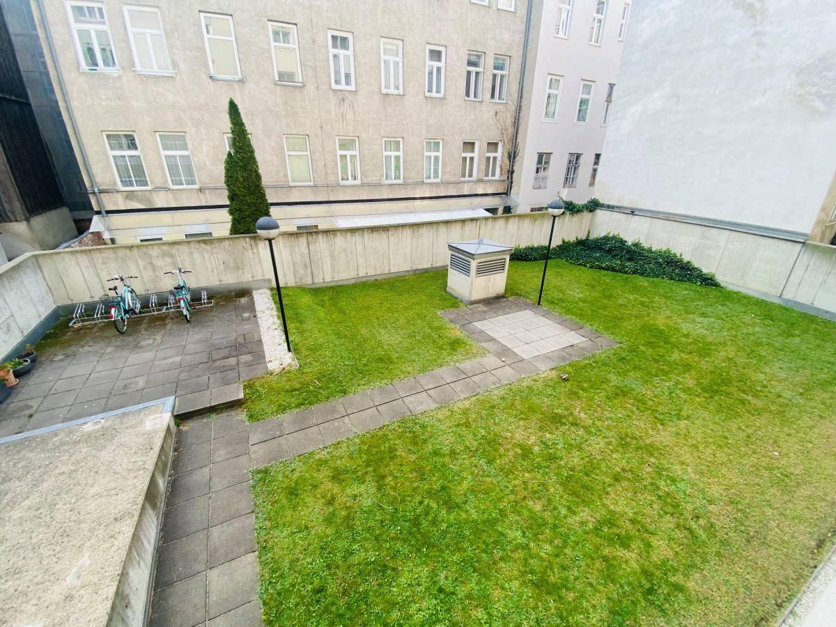 Gemeinschaftsgarten mit Rasenfläche, gepflasterten Wegen und Fahrradstellplätzen.
