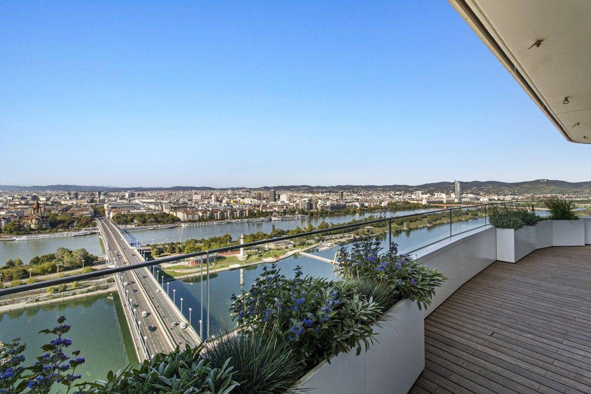 Geräumige Terrasse mit Holzdeck, Glasgeländer und Pflanzen, bietet einen weiten Stadt- und Flussblick.