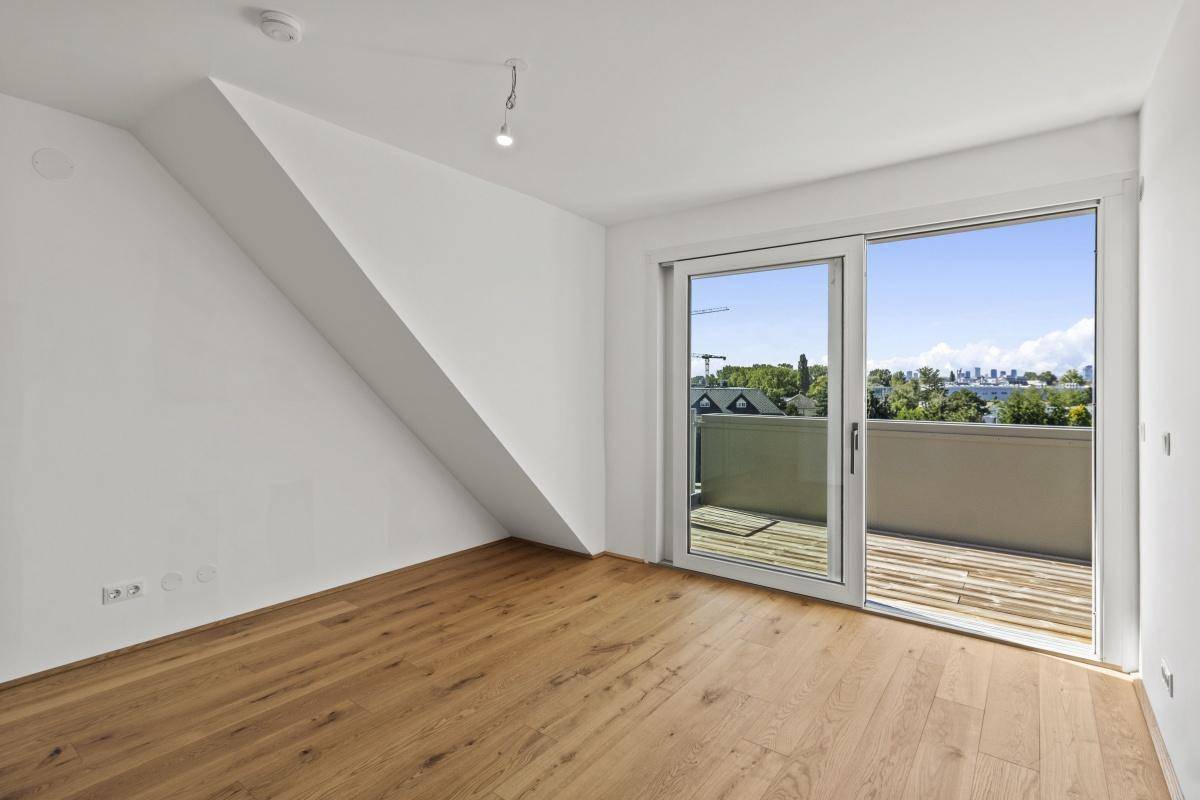 Helles Schlafzimmer mit Holzboden, schräger Wand und Zugang zum Balkon.