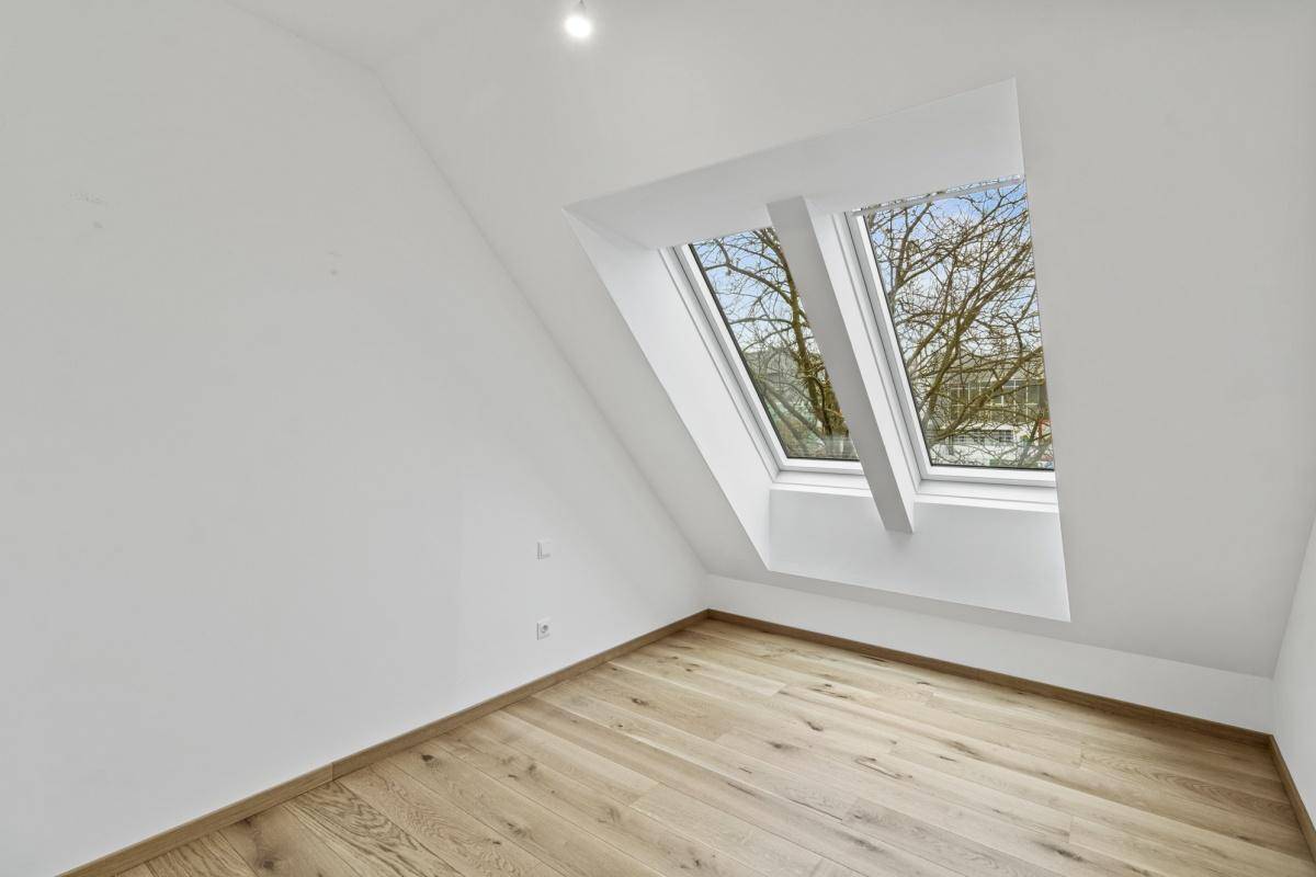 Helles Zimmer mit Holzboden, schrägen Wänden und zwei Dachfenstern, die eine angenehme Wohnatmosphäre bieten.