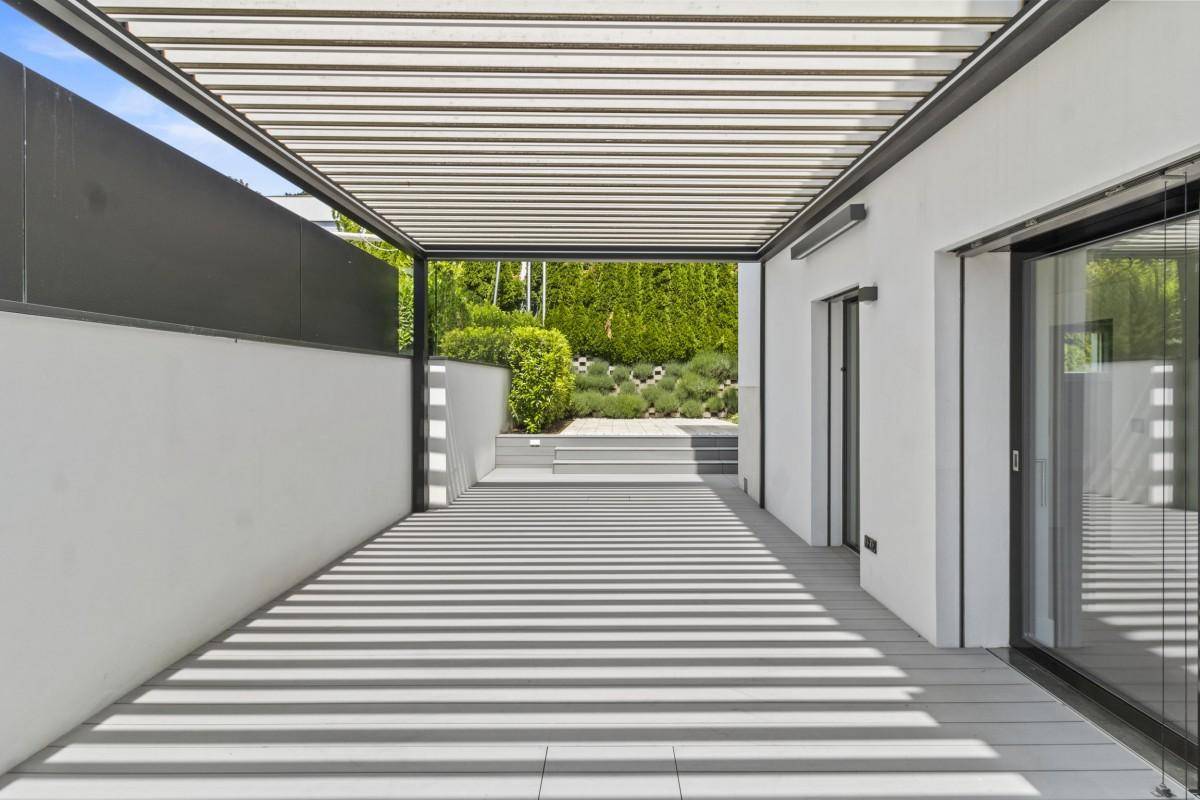 Überdachte Terrasse mit Lamellenpergola und Zugang zu einem gepflegten Gartenbereich.