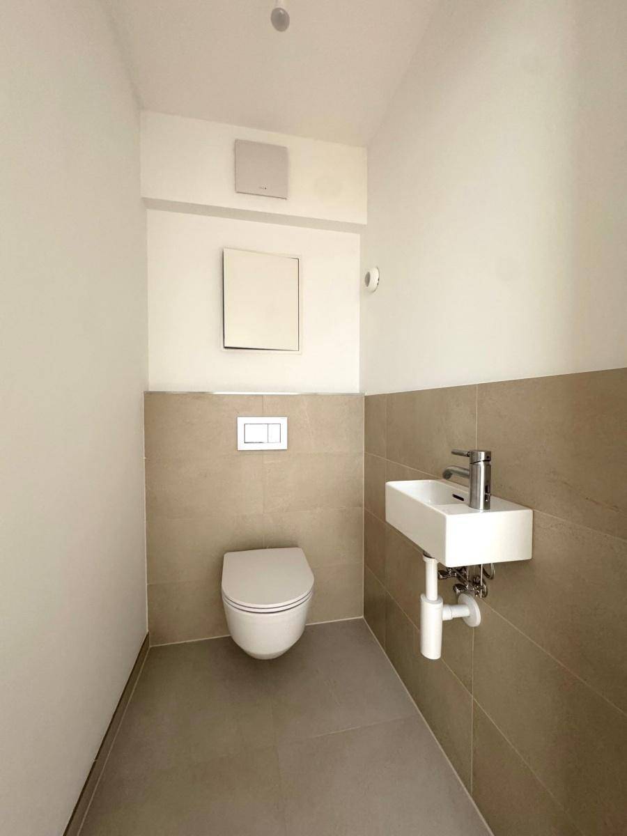 Modernes Gäste-WC mit wandhängender Toilette, kleinem Waschbecken und beigefarbenen Fliesen.