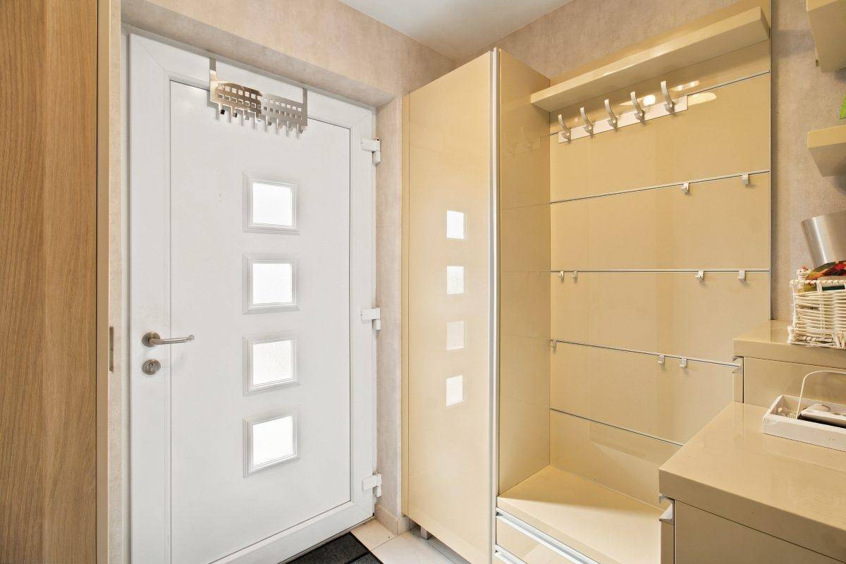 Eingangsbereich mit heller Garderobe, Spiegelflächen und weißer Eingangstür.