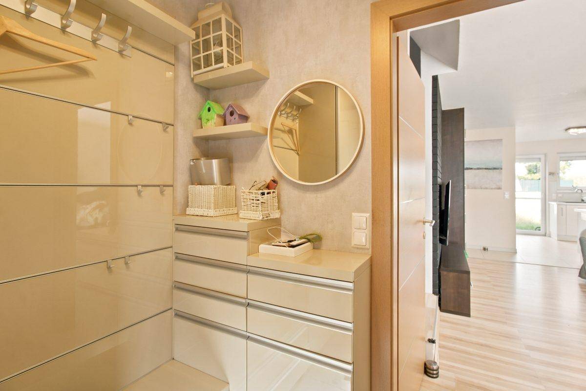 Moderner Flur mit integrierter Garderobe, Spiegel und Blick in den offenen Wohnbereich.