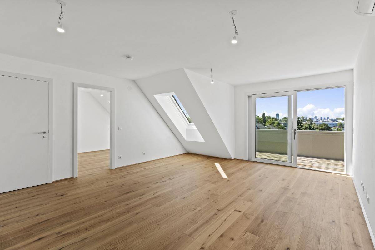 Heller Wohnraum im Dachgeschoss mit Holzboden, Dachfenster und Balkonzugang.