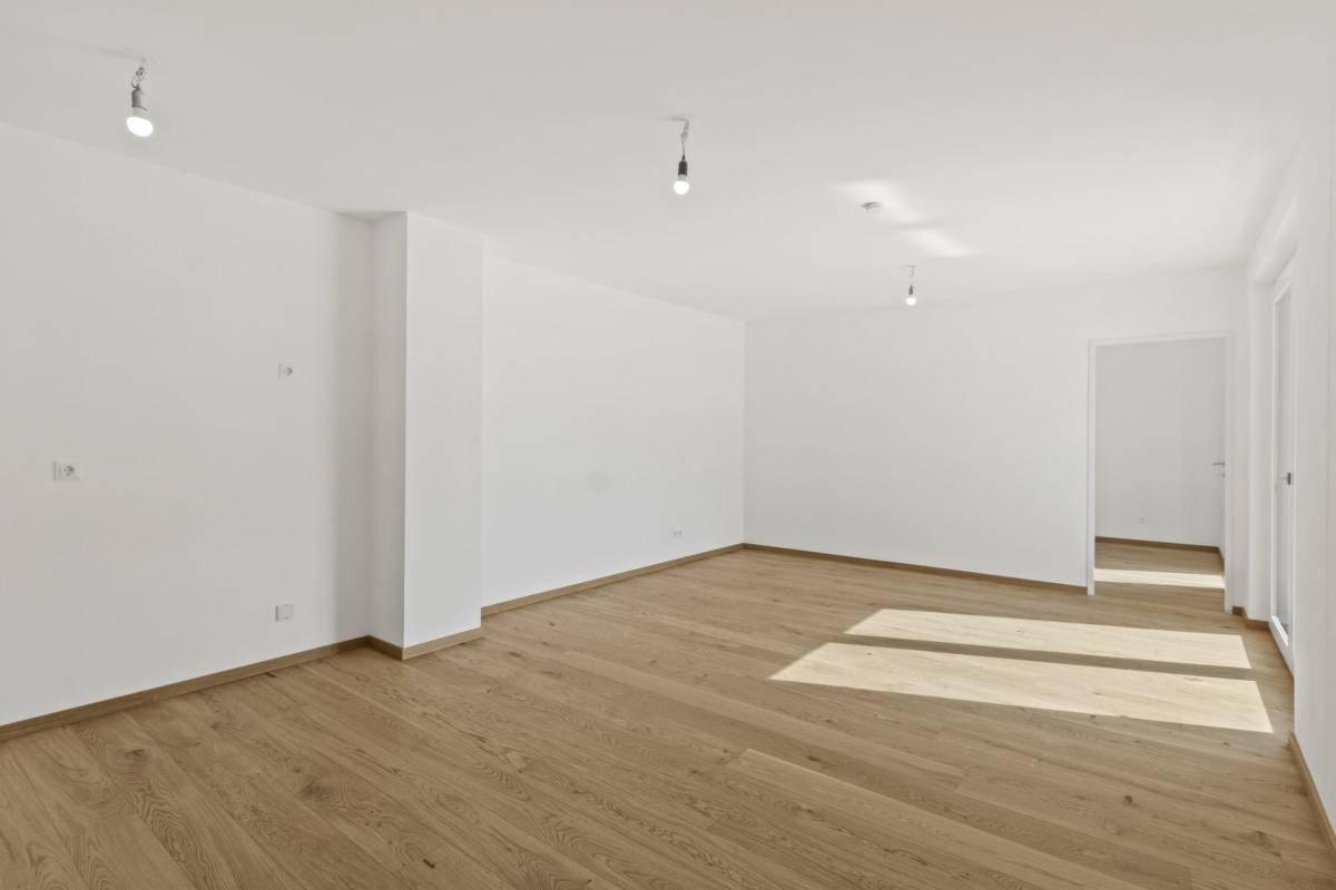 Helles, leeres Wohnzimmer mit neuem Holzparkettboden und weißen Wänden.
