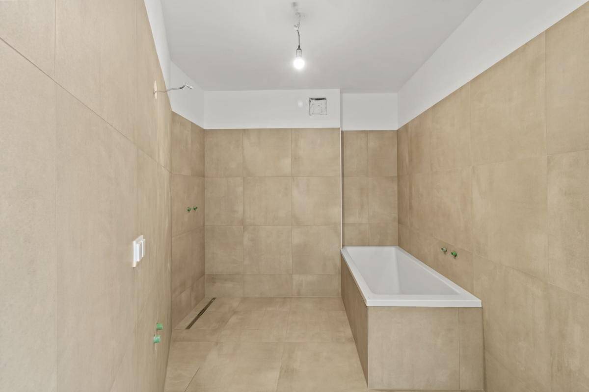 Unfertiges Badezimmer mit beigefarbenen Fliesen, Badewanne und vorbereitetem Duschbereich.